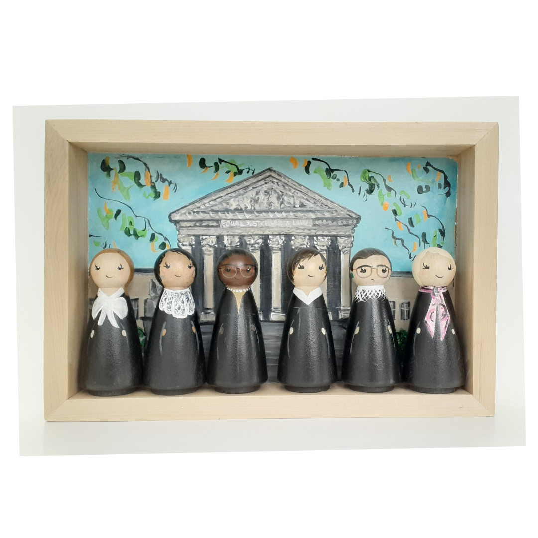 Wooden peg dolls painted as the Female Judges of the Supreme Court standing in front of original painting of Supreme Court